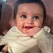 Mila is registered to the contest to win money with this photo: baby, child, smile, face, hand, eyes, cushion, soft_fabric, indoor, window, sunlight, shadow, long_eyelashes, clothing, cheeks, portrait, happy, infant, cute, close_up