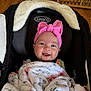 Oakley is registered to the contest to win money with this photo: baby, infant, child, car_seat, headband, pink_bow, blanket, smile, happy, face, cheeks, eyes, graco_logo, stroller, plush_blanket, clothing, portrait, indoors, wood_floor, seat