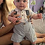Grayson is registered to the contest to win money with this photo: baby, child, person, clothing, shorts, suspenders, hand, face, eyes, room, bed, adult, skin, footwear, decor, artwork, butterfly, purple_wall, indoor, portrait