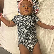 Essence joined the competition — help win amazing prizes! baby, infant, onesie, headband, lying_down, curious, indoor, blanket, soft_surface, patterned_clothing, arms_outstretched, child, person, cute, young_child, baby_clothes, cozy, resting, looking_at_camera, home