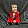 baby, black_buttons, black_feet, child, clothing, cute, expression, fabric_background, face, festive, hands, holiday, indoors, looking_up, portrait, red_outfit, santa_costume, sitting, smiling, young_child