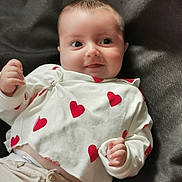 Colin a rejoint le concours — aidez-le/la à gagner de superbes lots ! baby, infant, smiling, white_shirt, red_hearts, beige_pants, hand, face, lying_down, cute, child, portrait, fabric_background, clothing, young, human, skin, head, eyes, expression