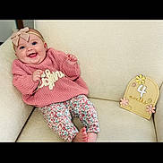 Leighnora joined the competition — help win amazing prizes! baby, smiling, pink_sweater, floral_pants, headband, bow, armchair, cream_color, wooden_sign, 4_months, decorative_flowers, happy, infant, cute, child, portrait, indoor, comfortable, clothing, young