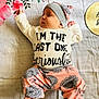 Gemma is registered to the contest to win money with this photo: baby, infant, child, floral_pattern, blanket, clothing, hat, pants, foot, face, cute, lying_down, text_on_clothing, pink, gray, white, home, indoors, person, portrait