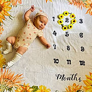 Gemma is registered to the contest to win money with this photo: baby, infant, blanket, sunflower, numbers, months, onesie, hat, socks, lying_down, cute, adorable, pattern, flower_wreath, age_marker, child, portrait, soft_texture, colorful, decorative
