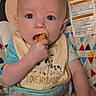 baby, infant, child, portrait, sitting, bouncer, bib, snack, eating, hand, face, eyes, smiling, indoor, close_up, colorful, patterned, baby_gear, safety_label, adorable