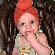 Nathanaelle a rejoint le concours — aidez-le/la à gagner de superbes lots ! baby, infant, child, turban, orange_headwear, flower_pattern, clothing, seat, cushion, brown, hand, fingers, face, eyes, cute, innocent, indoor, person, closeup, portrait