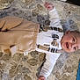 baby, child, smiling, lying_down, suspenders, bow_tie, pants, white_shirt, patterned_surface, quilted_mat, blue_mat, happy, infant, indoor, cute, person, face, clothing, head, toddler