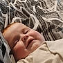 baby, child, face, smile, cheeks, blanket, pattern, clothing, infant, lying_down, cute, happy, bed, soft, skin, head, young, portrait, indoors, person