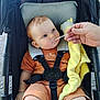 baby, black_stroller, blanket, child, childcare, curious_expression, cute, daylight, feeding, feeding_time, hand, infant, orange_clothing, outdoor, portrait, seatbelt, sitting, spoon, stroller, yellow_blanket