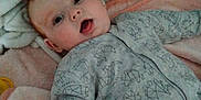 Scott is registered to the contest to win money with this photo: baby, bed, blanket, blue_toy, child, crib, cute, dinosaur_pattern, expression, face, hand, indoors, infant, mouth_open, onesie, pink_blanket, sleeping_area, sleepwear, soft_toys, white_blanket