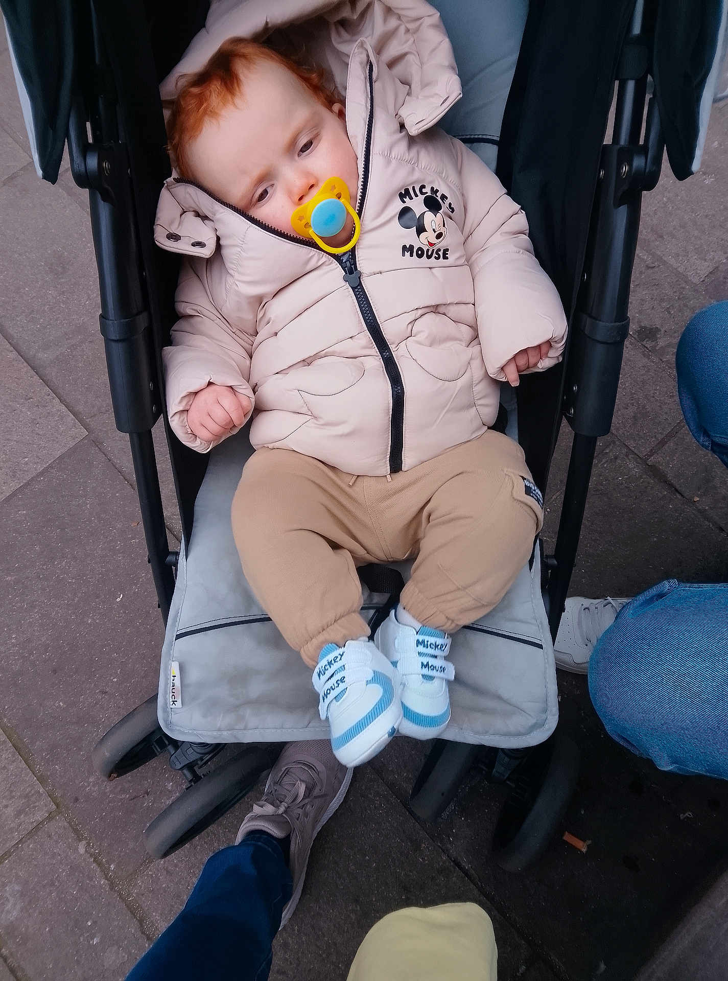 Scott joined the competition — help win amazing prizes! baby, child, stroller, pacifier, jacket, mickey_mouse, footwear, pavement, urban, person, clothing, casual, winter, outdoor, cute, infant, sitting, hooded, shoes, legs