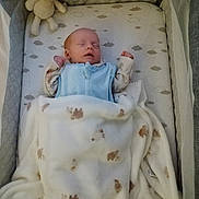 Scott is registered to the contest to win money with this photo: baby, sleeping, crib, blanket, plush_toy, reindeer, pajamas, infant, cozy, soft, cushion, pattern, animal_print, bed, rest, child, nursery, peaceful, indoors, cute