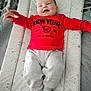 baby, child, red_sweatshirt, grey_pants, striped_socks, smiling, lying_down, cushioned_mat, patterned_mat, indoor, happy, cute, infant, reaching_out, cozy, soft_toys_pattern, casual_clothing, person, portrait, home