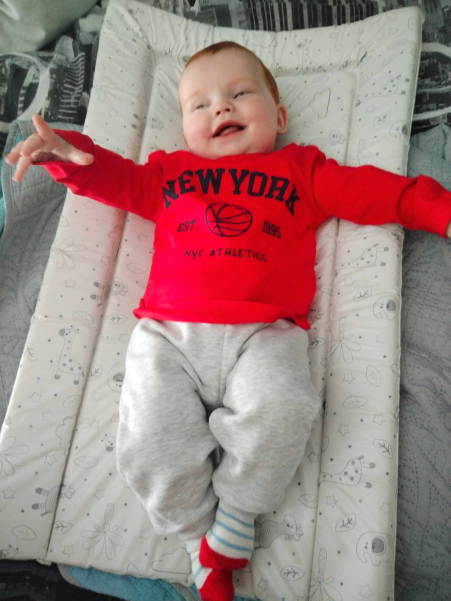 Scott joined the competition — help win amazing prizes! baby, child, red_sweatshirt, grey_pants, striped_socks, smiling, lying_down, cushioned_mat, patterned_mat, indoor, happy, cute, infant, reaching_out, cozy, soft_toys_pattern, casual_clothing, person, portrait, home