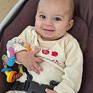 Cléo participe au concours pour gagner de l'argent avec cette photo : baby, infant, child, car_seat, safety_harness, toy, colorful_toy, blue_eyes, cream_outfit, smiling, happy, indoor, wooden_background, cute, hands, face, seated, comfortable, young, portrait