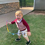 Jaxon joined the competition — help win amazing prizes! child, toddler, playing, outdoor, grass, ribbon, happy, smiling, sunlight, casual_clothing, shorts, jacket, barefoot, fun, daytime, two_children, lawn, running, joy, playtime