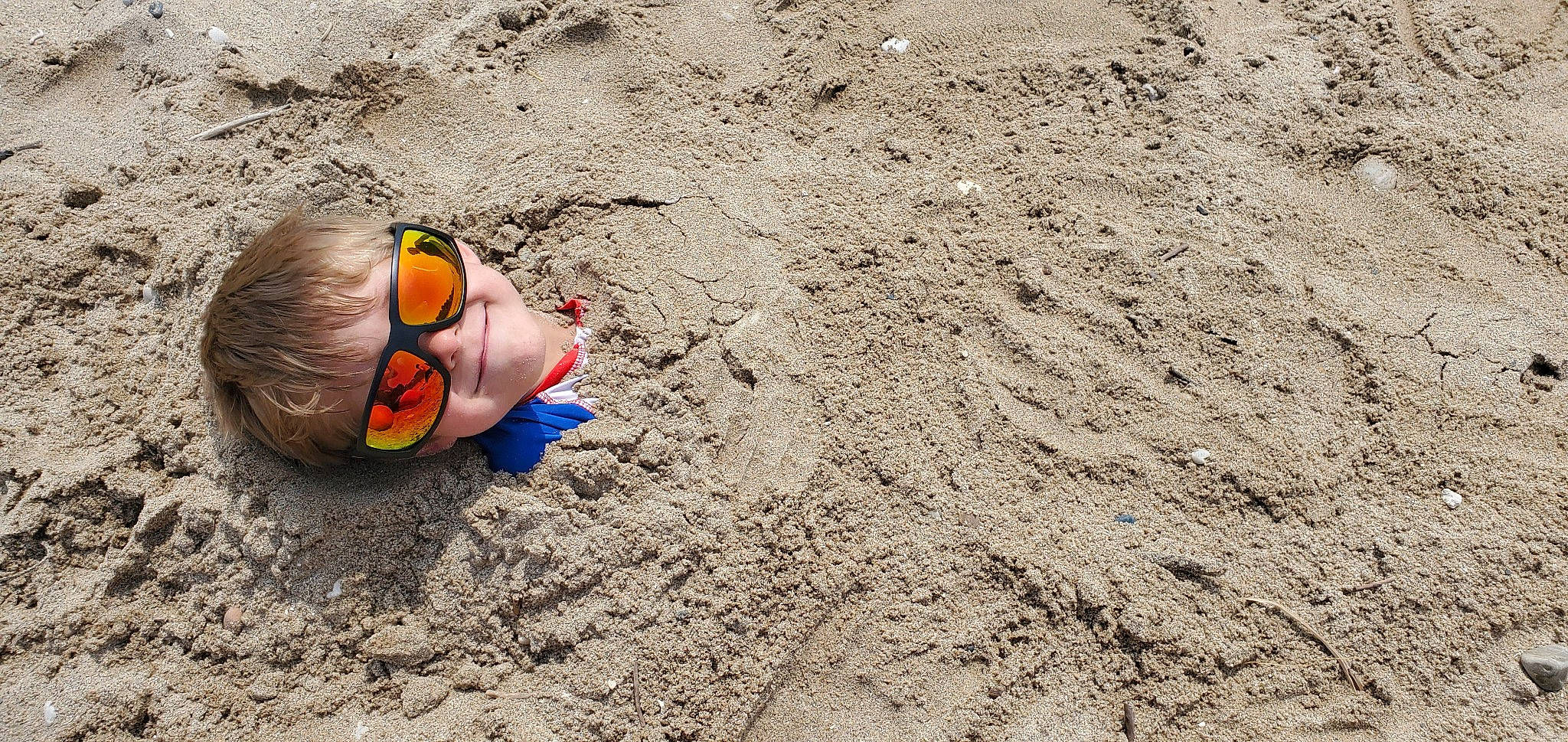 James is registered to the contest to win money with this photo: beach, eyewear, fun, grass, human_leg, landscape, leisure, person, personal_protective_equipment, recreation, rock, sand, shadow, soil, wood