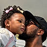 toddler, child, man, kiss, affection, curly_hair, bow, earrings, glasses, cap, close_up, portrait, indoor, love, family, skin, beard, black_clothing, cute, affectionate