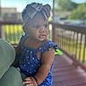 toddler, child, headband, bow, blue_clothing, outdoor, porch, railing, daylight, curious_expression, person, infant, hand, patterned_clothing, summer, skin, face, portrait, holding, adult