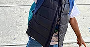 Samir is registered to the contest to win money with this photo: child, boy, outdoor, sidewalk, grass, backpack, black_vest, white_tshirt, blue_jeans, blue_crocs, pose, playful, person, footwear, casual_clothing, street, young, confident, smiling, daylight
