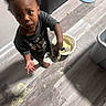 Tiny is registered to the contest to win money with this photo: toddler, child, barefoot, floor, food, messy, shoe, indoor, looking_up, curious, hand, face, expression, container, lid, clothing, footwear, person, home, spill