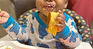 Tiny joined the competition — help win amazing prizes! baby, blurred_background, carrots, child, cornbread, crumbs, eating, face, food, hand, happy, high_chair, indoor, mouth, onesie, orange, person, polka_dot, seated, tray