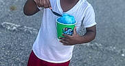 Tiny joined the competition — help win amazing prizes! child, smiling, shaved_ice, blue_treat, green_cup, white_tshirt, red_shorts, blue_crocs, outdoor, pavement, person, happy, summer, food, snack, casual_clothing, daytime, playful, young, standing