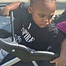 Tiny is registered to the contest to win money with this photo: activity, baby, black_shirt, casual_clothing, child, daylight, expression, hand, outdoor, person, portrait, seat, serious_face, skin, stroller, sunlight, toddler, transport, wheelchair, young_child