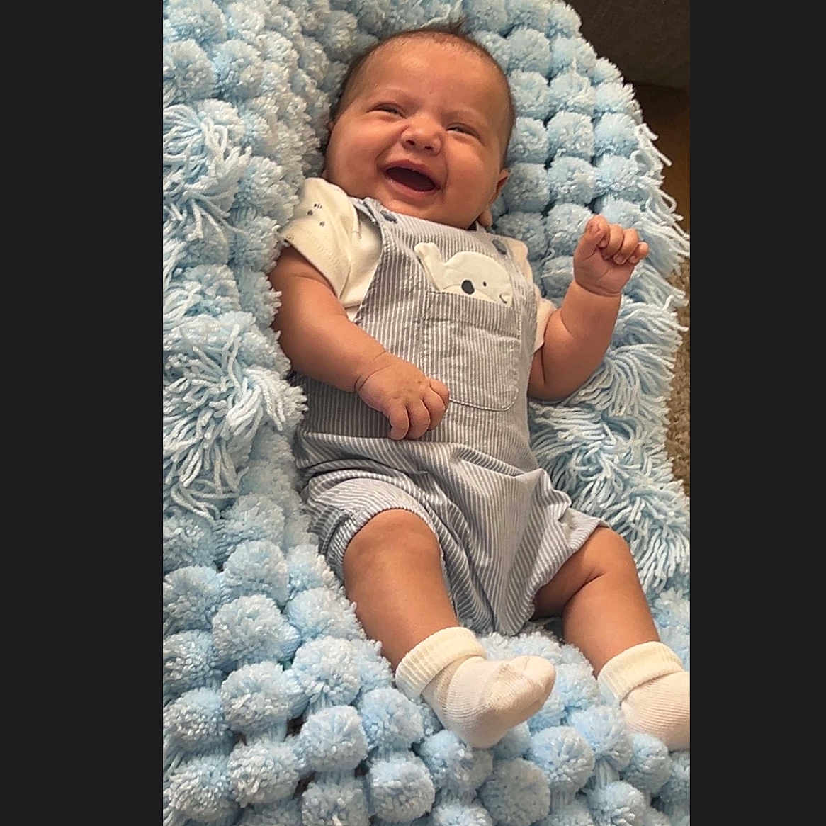 Elijah is registered to the contest to win money with this photo: baby, blanket, blue, child, clothing, comfort, cozy, cute, expression, fabric, happy, indoor, infant, overalls, portrait, resting, smiling, socks, soft, texture
