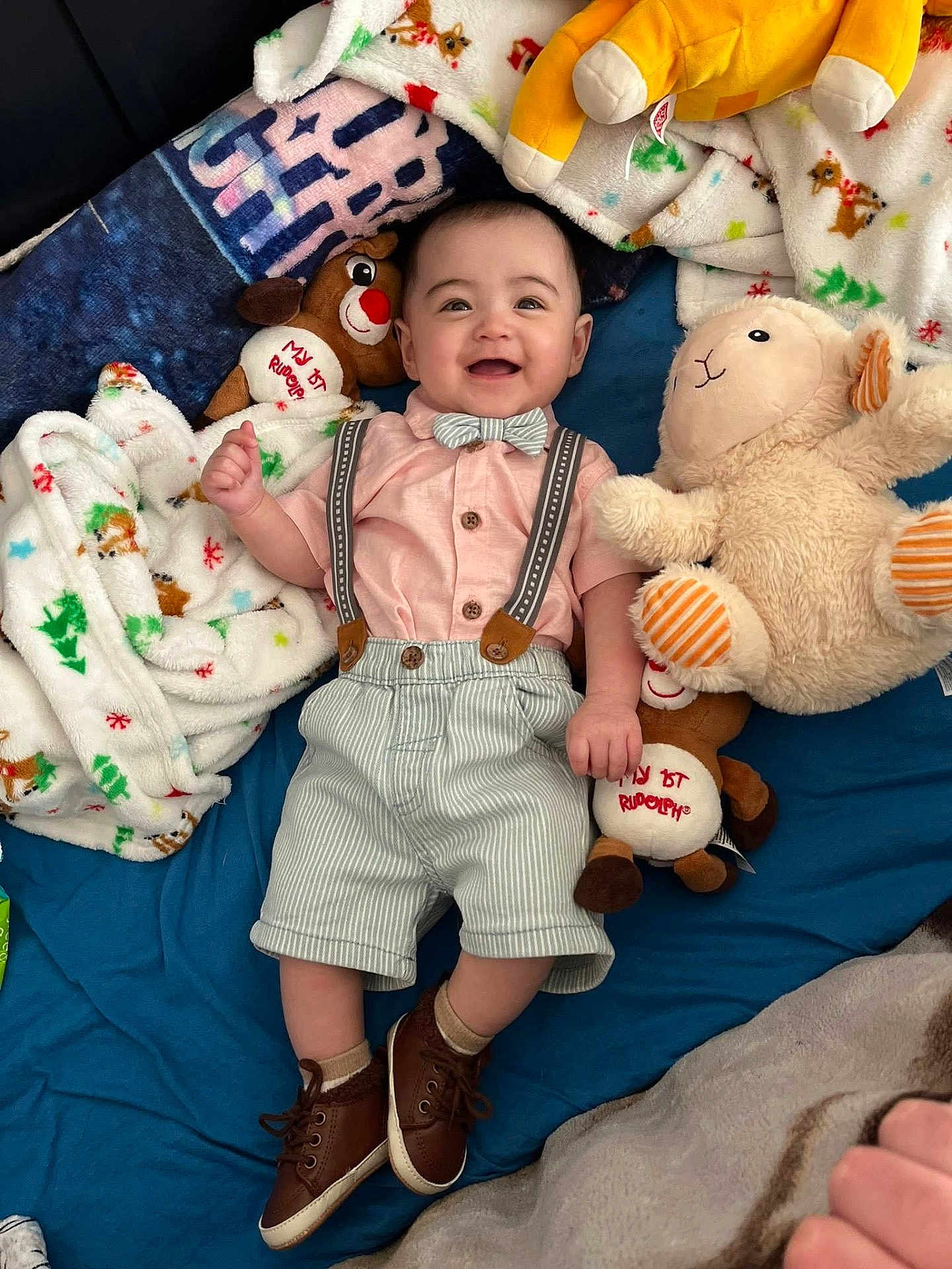 David joined the competition — help win amazing prizes! baby, child, smiling, plush_toy, blanket, clothing, bow_tie, suspenders, footwear, bed, happy, cute, indoor, person, soft_toy, reindeer_toy, lamb_toy, fabric, cushion, portrait