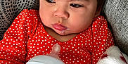 Phoebe is registered to the contest to win money with this photo: baby, bottle, milk, polka_dot, orange_clothing, blanket, hand, face, infant, cozy, texture, couch, portrait, indoors, young_child, sleepy, expression, holding, closeup, warm