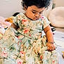baby, child, curly_hair, floral_dress, sitting, indoors, cute, thoughtful, soft_toys, home, floor_mat, bracelet, portrait, infant, toddler, person, childhood, pretty, calm, young