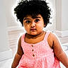 toddler, child, girl, curly_hair, pink_dress, polka_dot, indoor, portrait, cute, young_child, face, expression, sitting, minimalist_background, soft_lighting, curious, eyes, skin, hair, buttoned_dress
