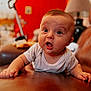 Emilio a rejoint le concours — aidez-le/la à gagner de superbes lots ! baby, infant, surprised, face, arms, leather, couch, indoor, red_background, expression, person, toddler, cute, skin, clothing, head, eyes, mouth, home, furniture