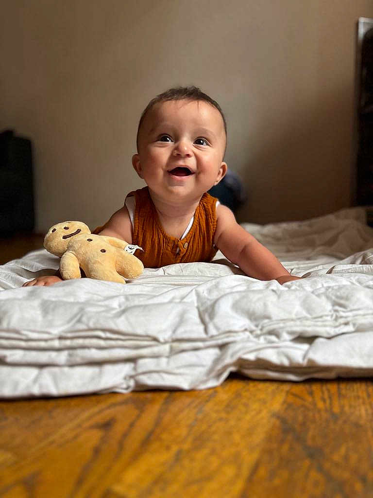 Emilio participe au concours pour gagner de l'argent avec cette photo : baby, child, smiling, indoor, plush_toy, quilt, wooden_floor, happy, face, portrait, crawling, cute, infant, clothing, brown_hair, toy, home, warm_lighting, expression, fabric