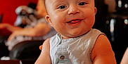 Emilio a rejoint le concours — aidez-le/la à gagner de superbes lots ! baby, smile, child, indoors, sitting, person, clothing, furniture, arm, face, head, buttoned_outfit, happy, skin, blurred_background, lamp, room, adult, table, comfort
