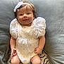 baby, smiling, white_dress, headband, puffed_sleeves, infant, cushion, pillow, soft_fabric, sitting, happy, indoors, cute, child, portrait, legs, hands, pattern, cozy, home