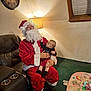 Aurora is registered to the contest to win money with this photo: baby, child, santa, santa_claus, beard, santa_hat, costume, living_room, lamp, recliner, couch, carpet, toy_mat, toy, holiday, christmas, glasses, portrait, indoor, sitting