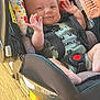 baby, car_seat, child, smiling, waving, infant, seatbelt, floral_pattern, wooden_floor, sunlight, happy, cute, indoors, clothing, person, face, hand, foot, safety, seat