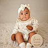 baby, infant, four_months, headband, bow, mittens, socks, cream_outfit, carpet, wooden_sign, portrait, cute, child, sitting, indoors, soft_lighting, neutral_background, smile, young_child, cozy