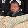 baby, infant, sleeping, blanket, car_seat, bow, clothing, face, child, cute, comfort, indoor, soft_lighting, peaceful, bundle, headwear, nap, closeup, rest, car