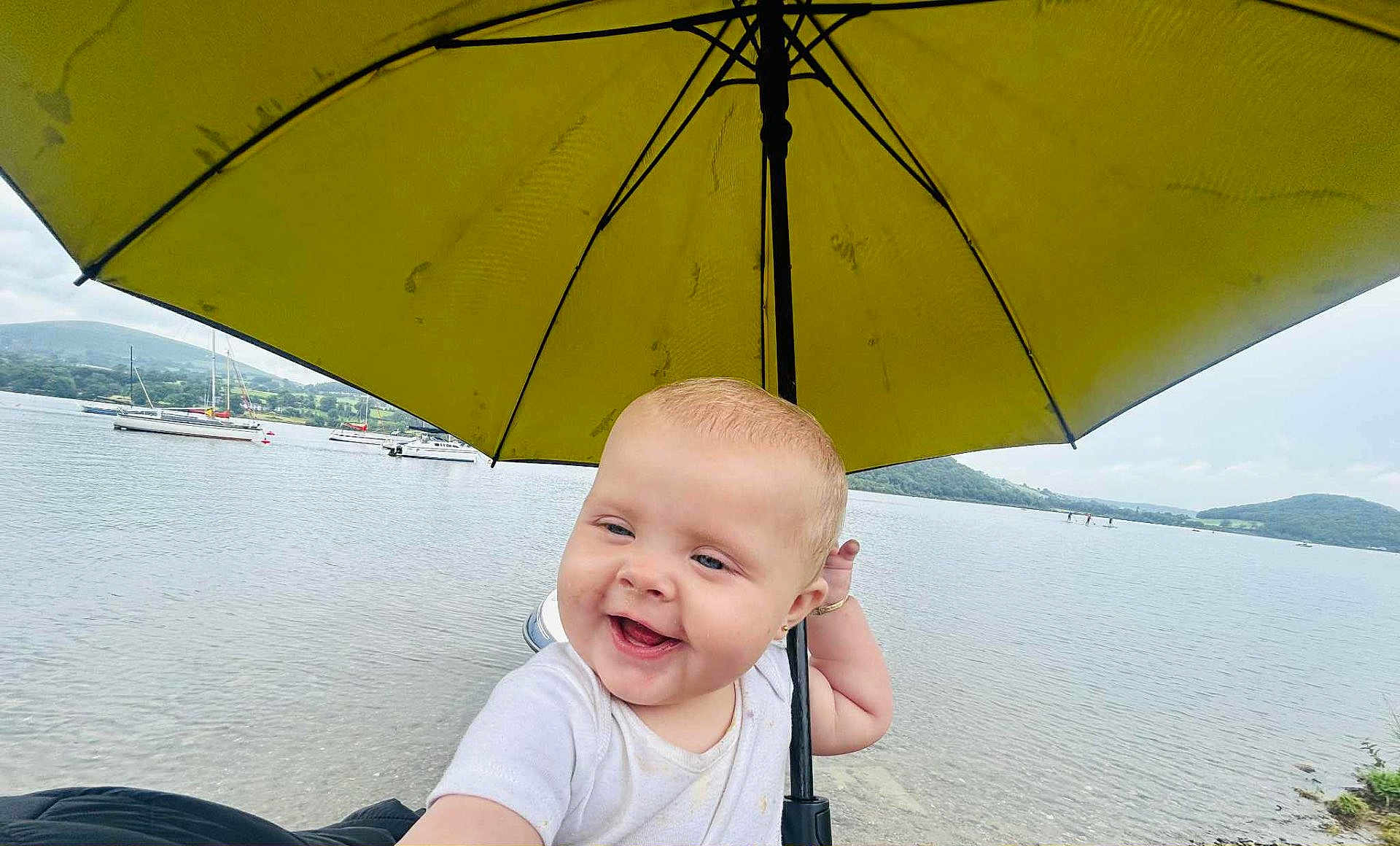 Veronica-Jade is registered to the contest to win money with this photo: baby, child, umbrella, yellow, lake, water, boats, outdoor, nature, hill, sky, cloudy, smiling, happy, portrait, person, summer, vacation, cute, scenic