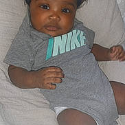 Jream joined the competition — help win amazing prizes! baby, infant, curly_hair, gray_onesie, nike, cushion, remote_control, indoor, child, cute, portrait, laying_down, skin, hand, fingers, face, eyes, nose, mouth, soft_fabric