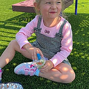 Gemini is registered to the contest to win money with this photo: casual_clothing, checkered_dress, child, cute, daytime, drink, fun, girl, grass, outdoor, park, pink_sweater, play_equipment, playground, shadow, shoes, sitting, smile, summer, sunlight