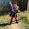 child, clown_costume, face_paint, swing, playground, outdoor, grass, boots, red_tights, black_skirt, hat, chains, fence, daylight, play, fun, smile, posing, costume, person