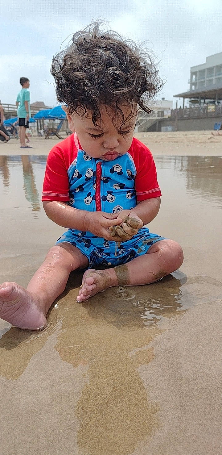 Marcellus is registered to the contest to win money with this photo: baby_toddler_clothing, barefoot, beach, blue, body_of_water, eye, fun, happy, leisure, people, person, pink, sand, shorts, skin, sky, summer, t_shirt, thigh, toddler
