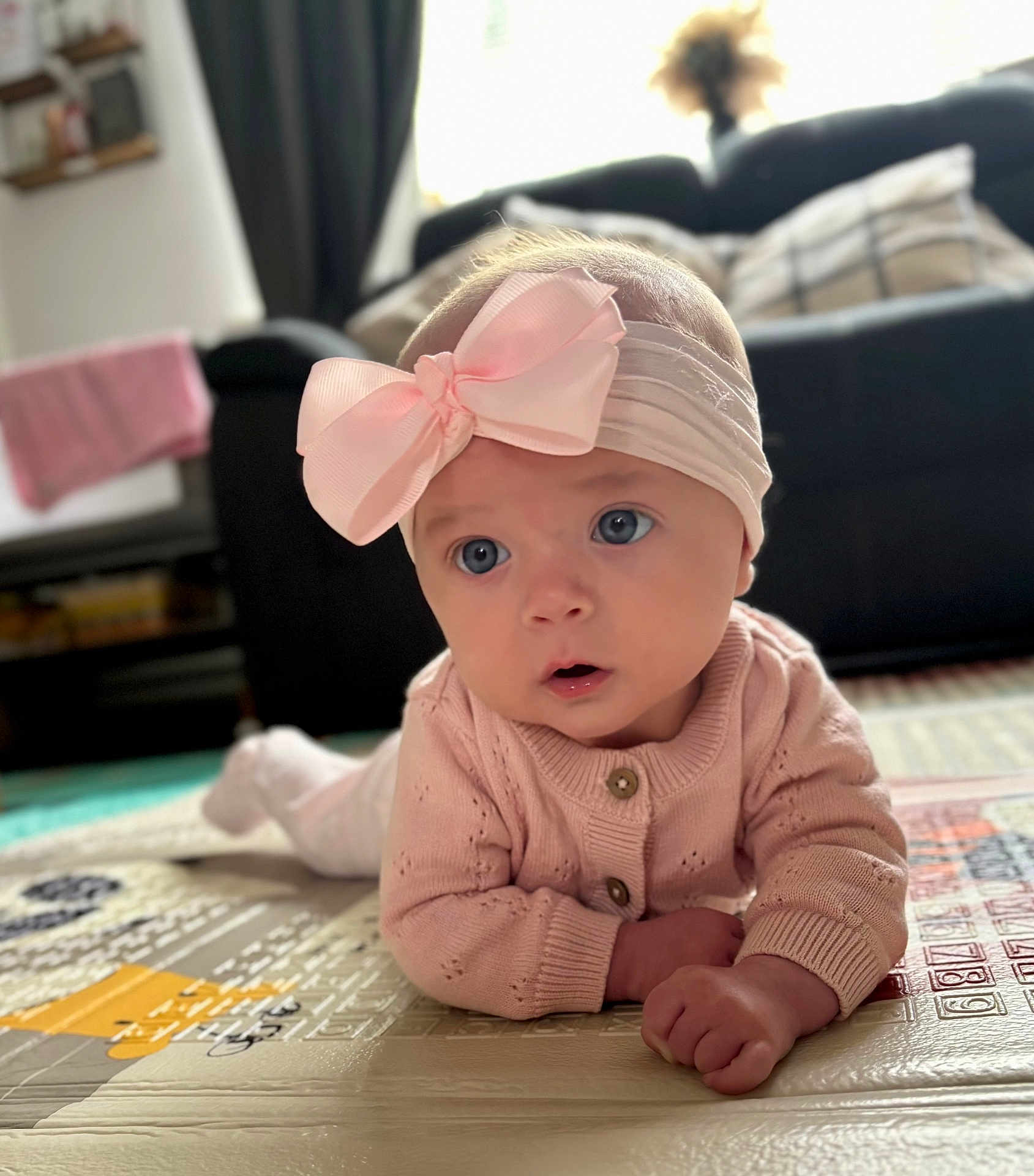 Violet joined the competition — help win amazing prizes! baby, blanket, blue_eyes, child, couch, curious, cute, floor, furniture, headband, indoors, infant, living_room, pink_bow, play_mat, portrait, soft_lighting, sweater, toddler, young_child
