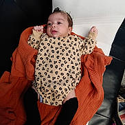 Renessmee joined the competition — help win amazing prizes! baby, infant, leopard_print, onesie, black_socks, orange_blanket, white_cushion, black_leather, person, child, lying_down, headband, indoors, soft_fabric, cute, skin, face, small_hands, expression, relaxed