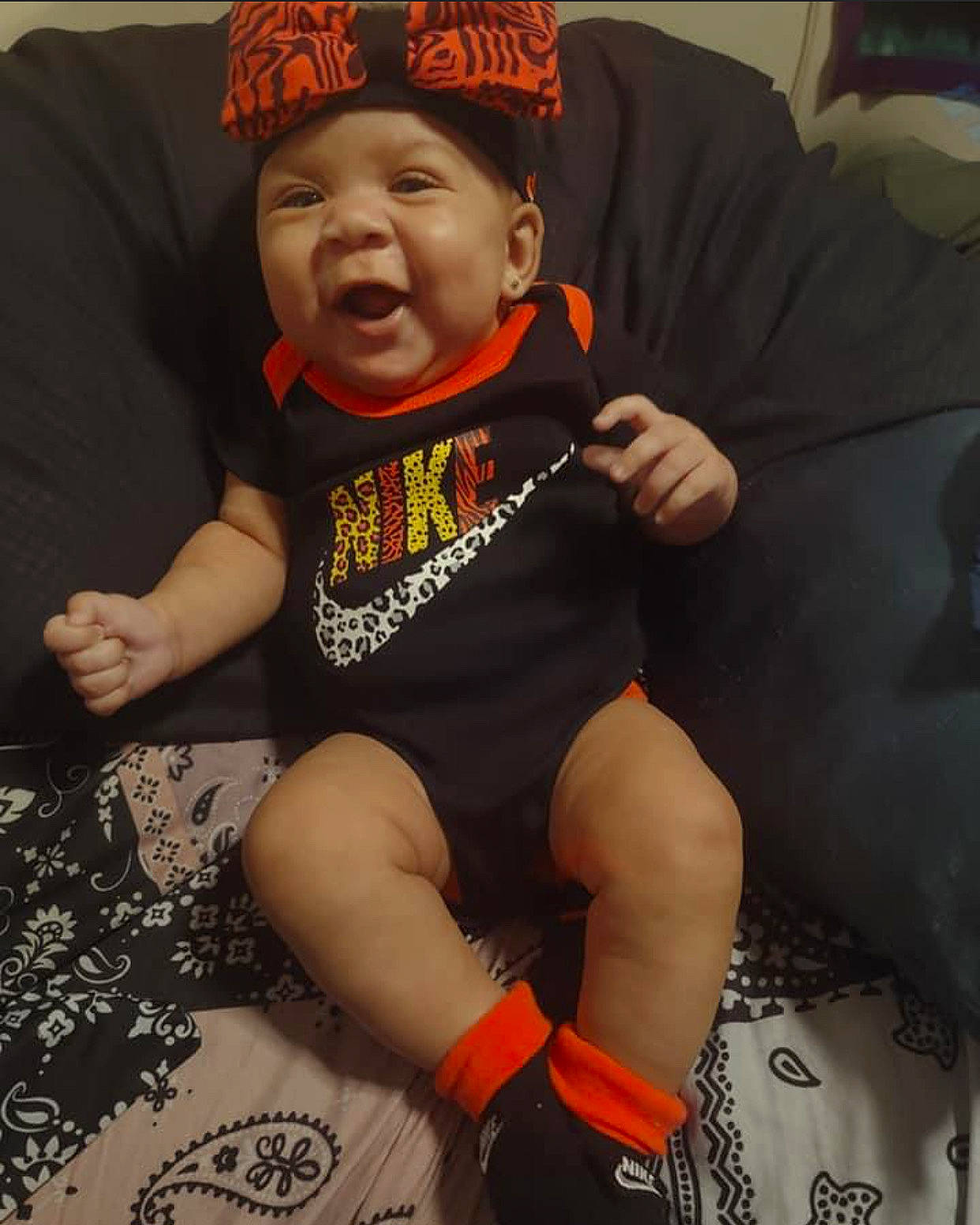 Khalani is registered to the contest to win money with this photo: baby_toddler_clothing, baseball_cap, cap, chair, comfort, cool, couch, face, happy, head, headwear, lap, leg, mouth, orange, person, shorts, sleeve, smile, t_shirt